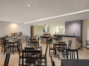 A spacious dining area with multiple tables and chairs, a central bar area, and a kitchen in the background. - Swiss-belinn Cibitung (Cikarang)
