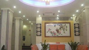 A hotel lobby with a central chandelier, a framed floral artwork, and a reception desk.