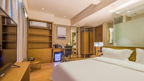 A hotel room with a large bed, a desk with a computer, a chair, a TV, and a wardrobe.