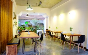 Un café moderno con mesas de madera, sillas blancas y negras, y vistas a un jardín.