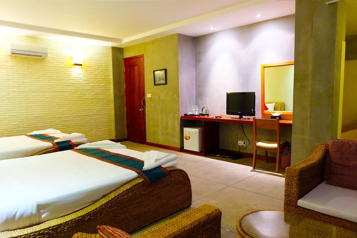 Quarto de hotel com duas camas, uma escrivaninha com computador, um pequeno frigorífico e uma cadeira.