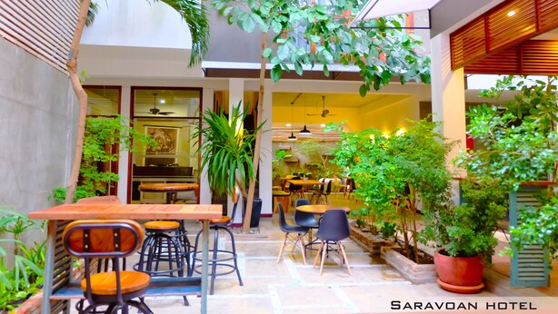 An indoor dining area with wooden tables and chairs, surrounded by potted plants and greenery. - Saravoan Royal Palace (Phnom Penh)