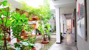 A hotel corridor with a water feature, potted plants, and a seating area. - Saravoan Royal Palace (Phnom Penh)