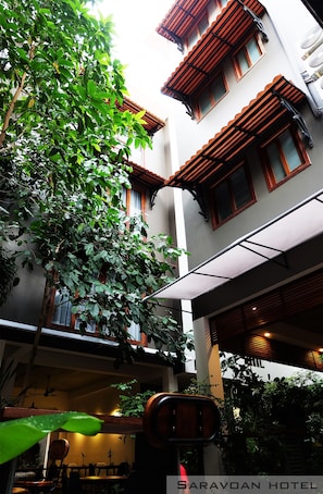 Un edificio de varios pisos con balcones, una zona de estar exterior cubierta y abundante vegetación.
