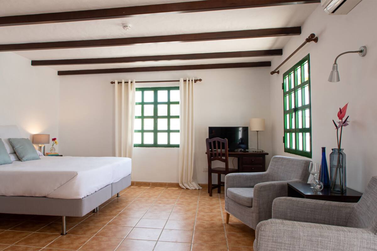A bedroom with a bed, a desk, a chair, a TV, and a window with green shutters.