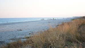 A beach with people and umbrellas, a boat in the distance, and tall grass in the foreground. - Castelvetere Hotel (Caulonia)