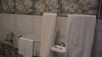 Une salle de bain avec trois serviettes blanches suspendues à un porte-serviettes, un support à papier toilette et une petite étagère sur laquelle reposent deux objets ronds.