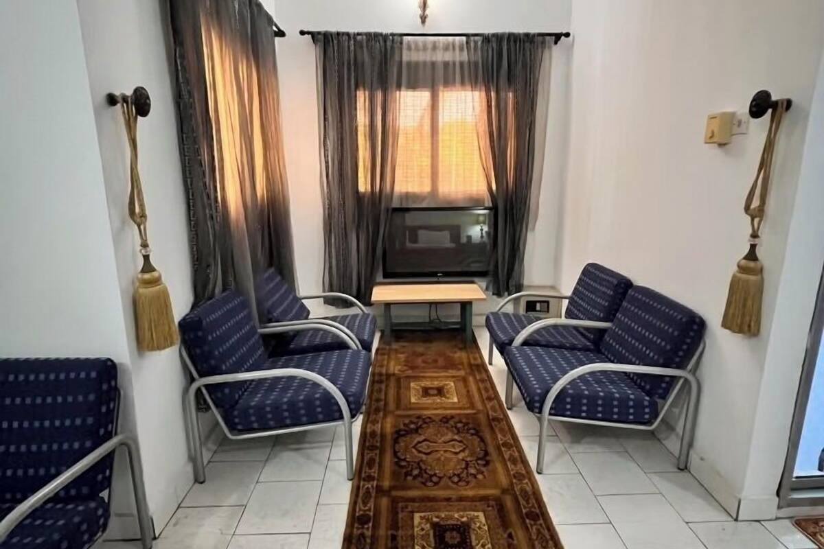 A room with a ceiling fan, two blue patterned sofas, a small table, and a patterned carpet.