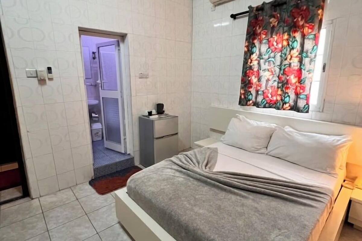 A bedroom with a large bed, a bathroom with a shower, and a door leading to a hallway.