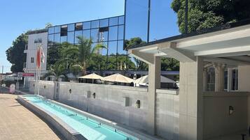 A swimming pool with a tiled deck, a building with a sign reading "Woodpecker Resort," and outdoor umbrellas.