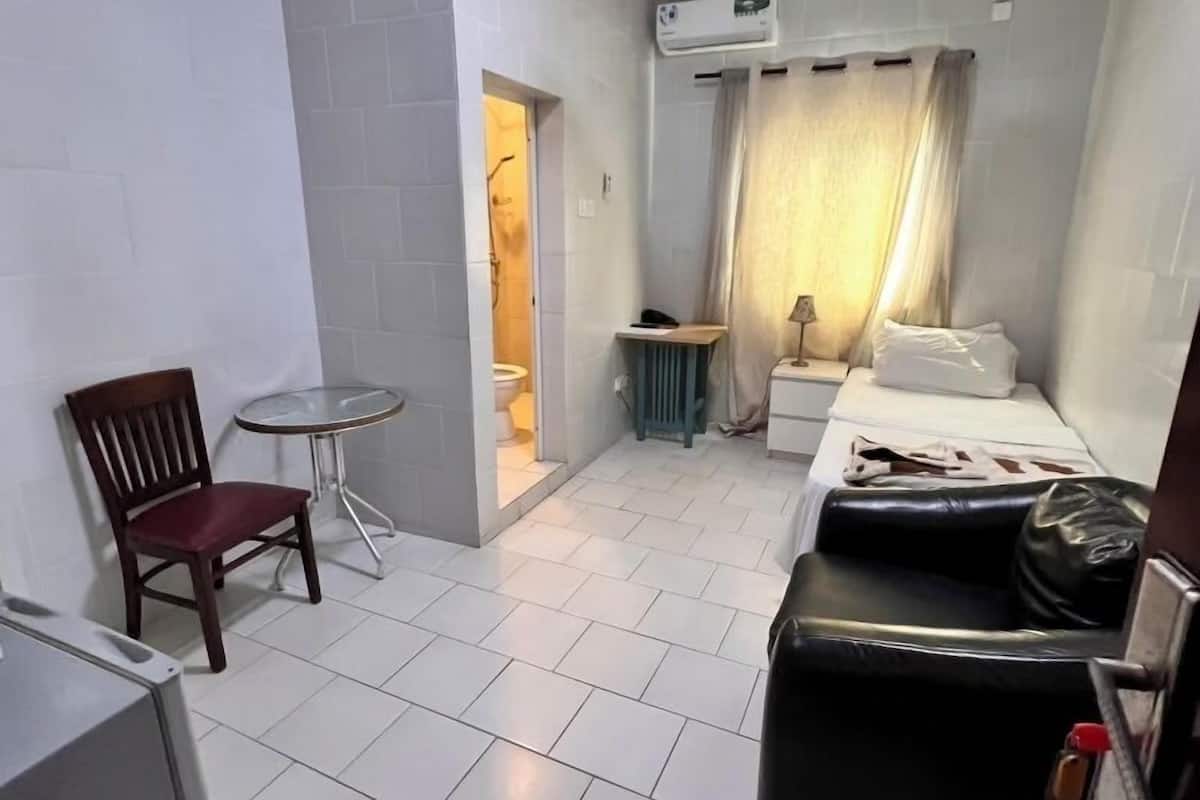 A compact hotel room with a bed, a small table, a chair, a sofa, and a ceiling fan.