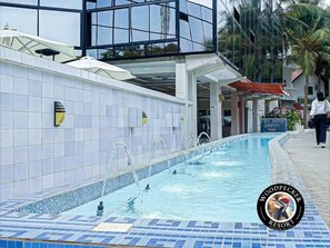 A swimming pool with a tiled edge, a sign for Woodpecker Resort, and a person walking by. - Woodpecker Resort (Banjulinding)