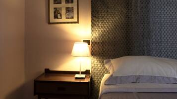 Een slaapkamer met een bed, nachtkastje, lamp en lijstjes met foto's aan de muur.