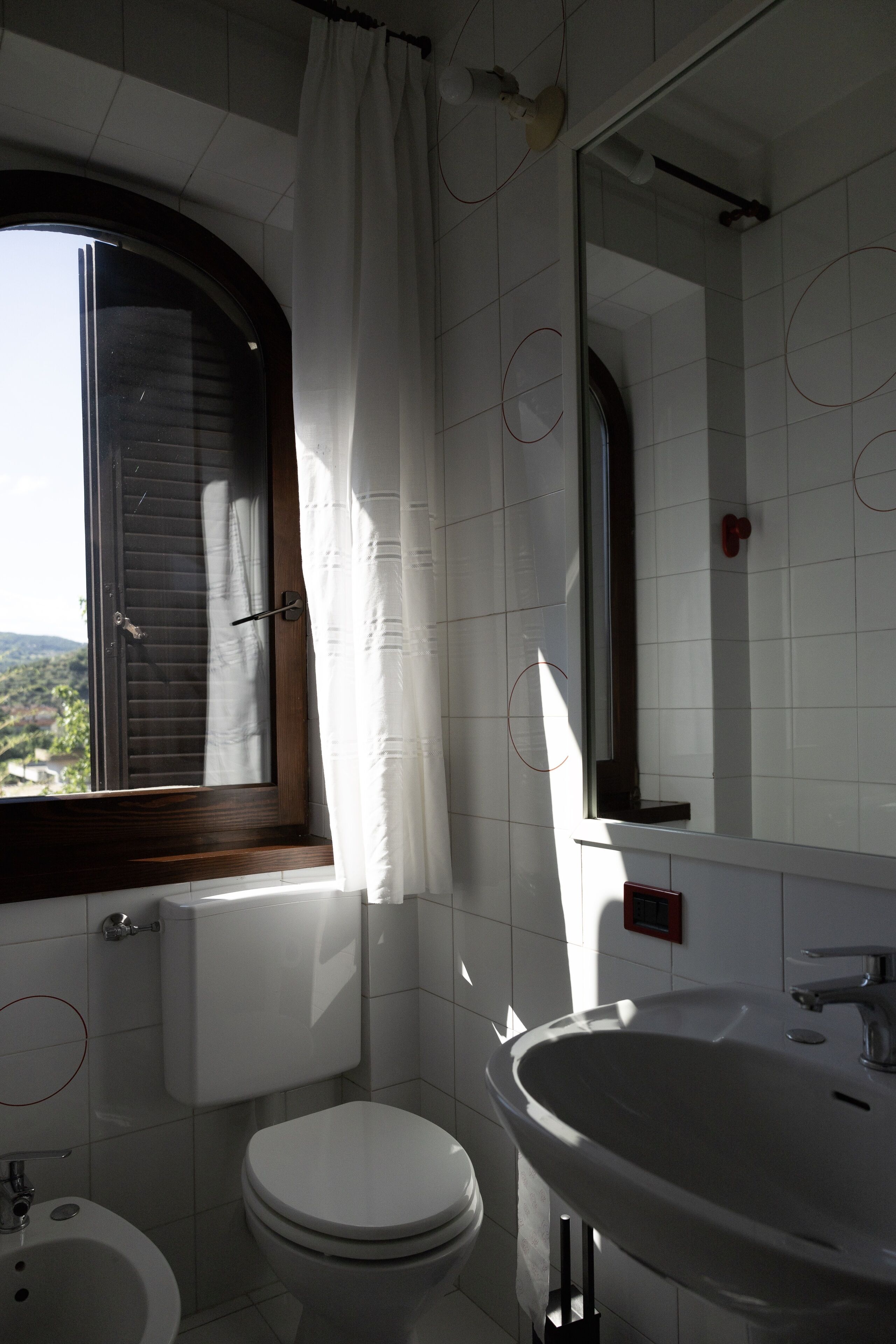 A bathroom with a toilet, sink, and window with curtains.