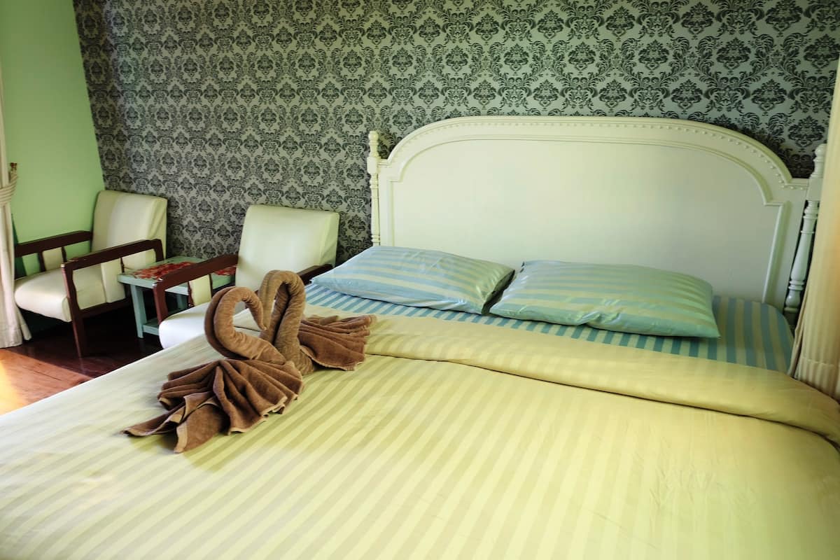A neatly made bed with striped bedding and two pillows, a brown towel, and a wooden headboard.