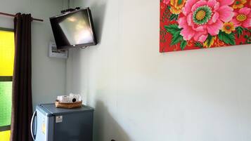 Une pièce avec un téléviseur fixé au mur, un réfrigérateur sur lequel est posé un panier, et un tableau représentant des fleurs accroché au mur.