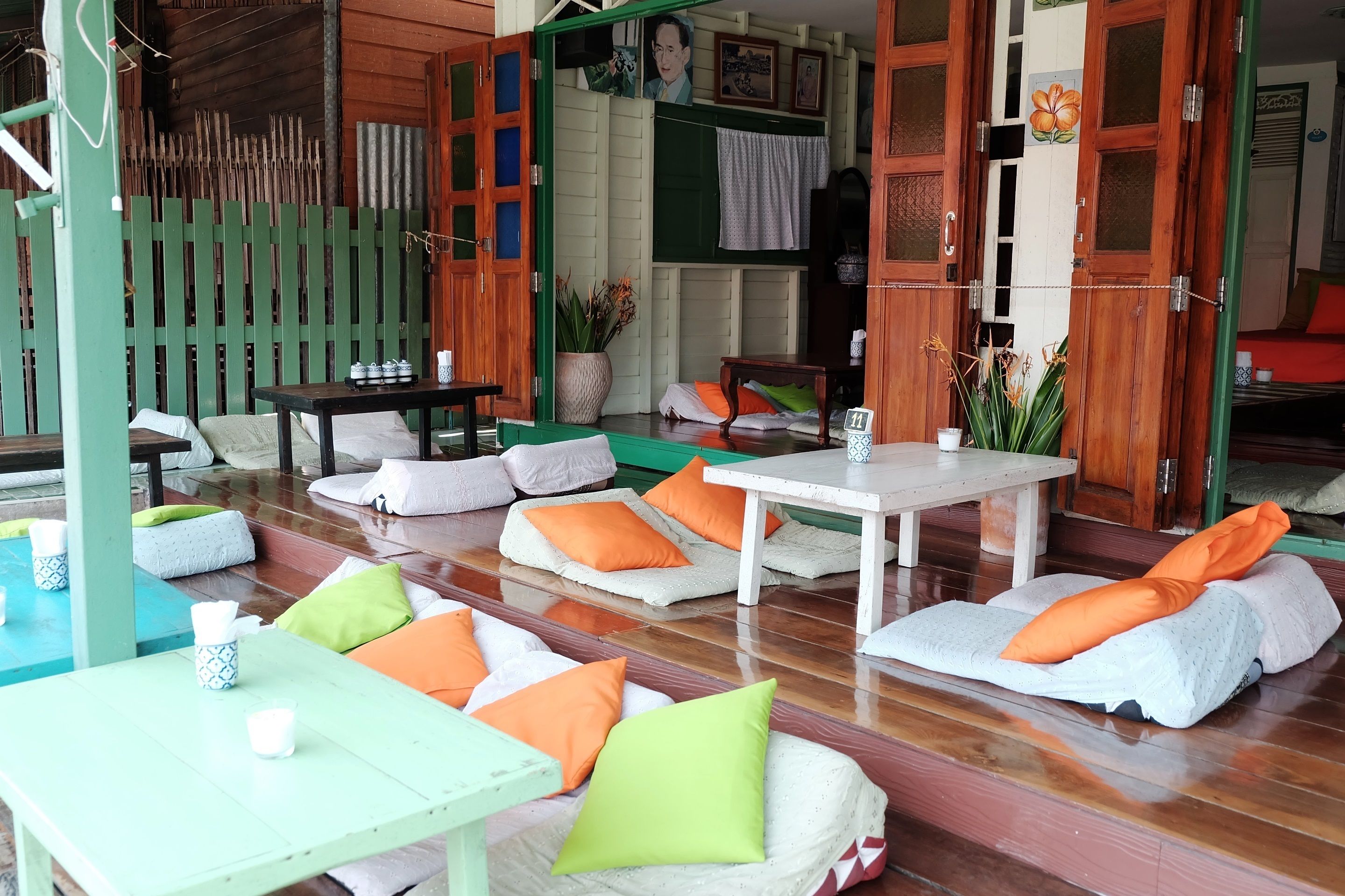 A cozy outdoor seating area with cushioned benches and tables, surrounded by wooden fences and a green backdrop.