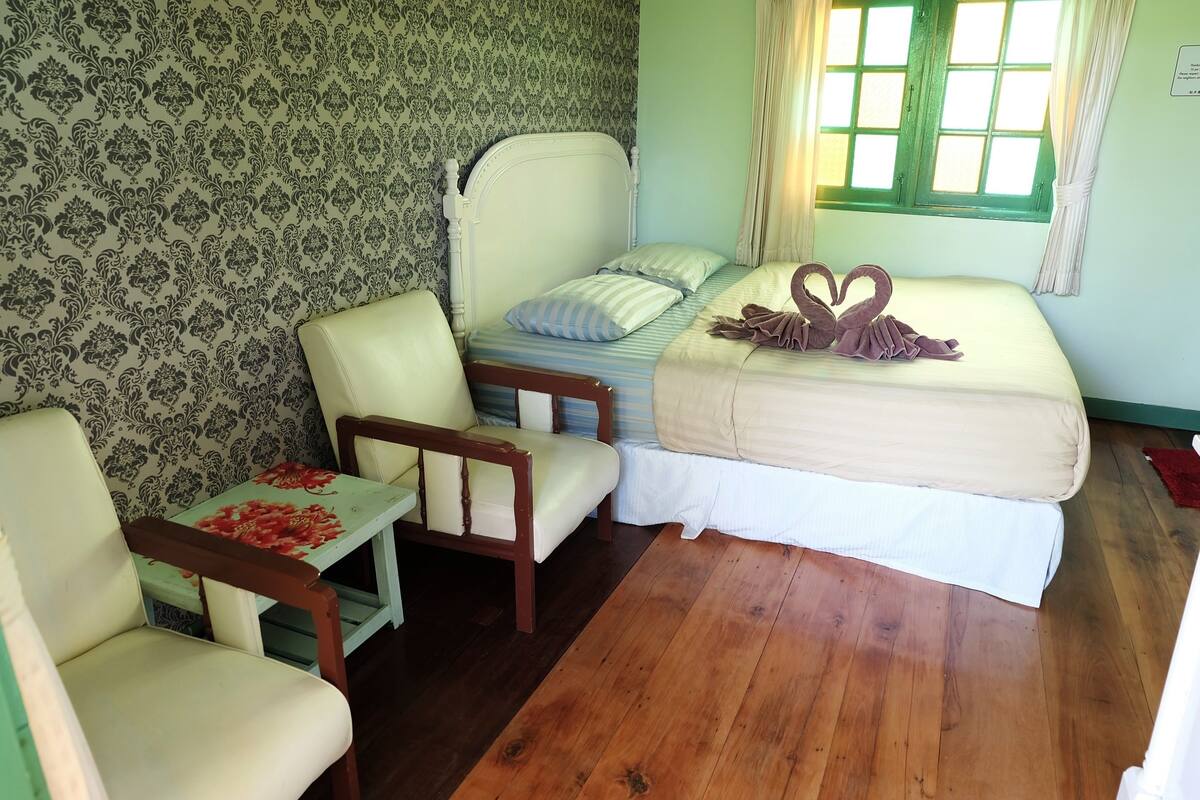 A room with a bed, a chair, a small table, and a window with curtains.