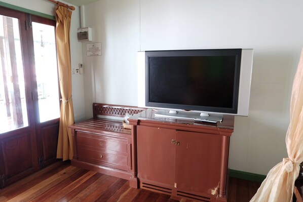 Una habitación con un armario de madera, un televisor encima y una ventana con cortinas.