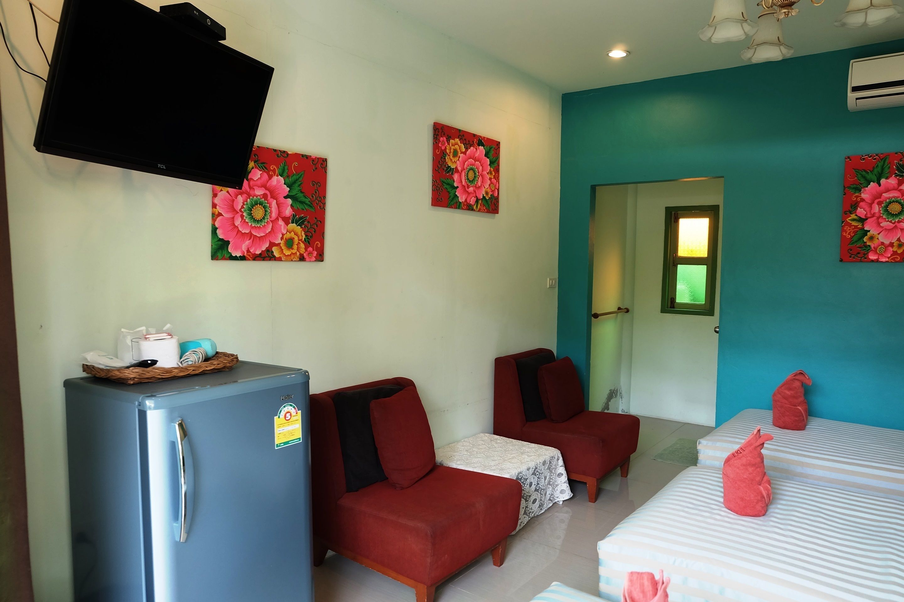 A room with a blue refrigerator, two red sofas, a bed with striped bedding, and a TV mounted on the wall.