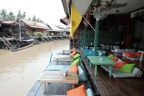 Un restaurante a orillas del río con mesas y bancos de madera, una bandera amarilla y un abanico.