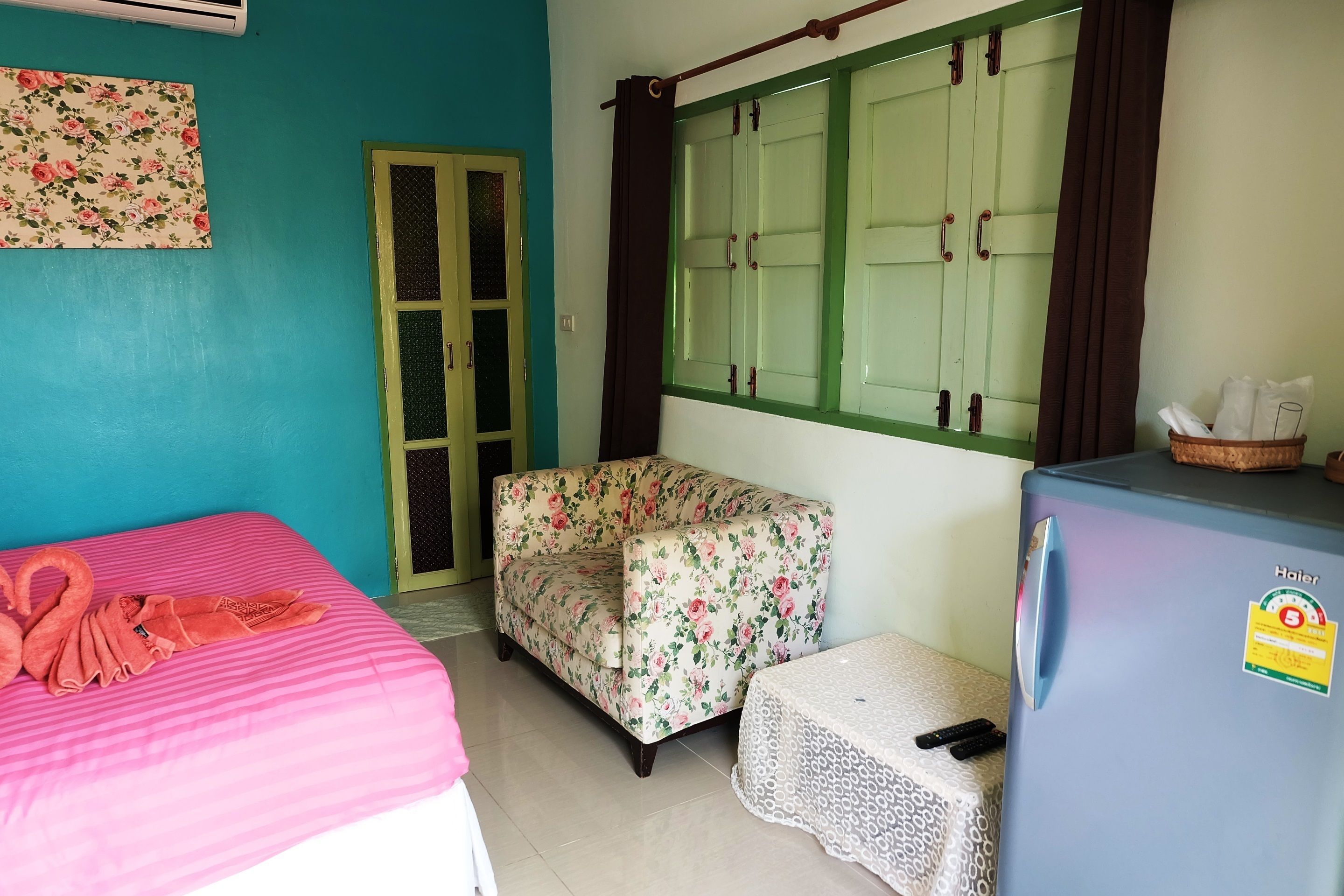 A room with a bed, a sofa, a table, a refrigerator, a window with curtains, and a door.
