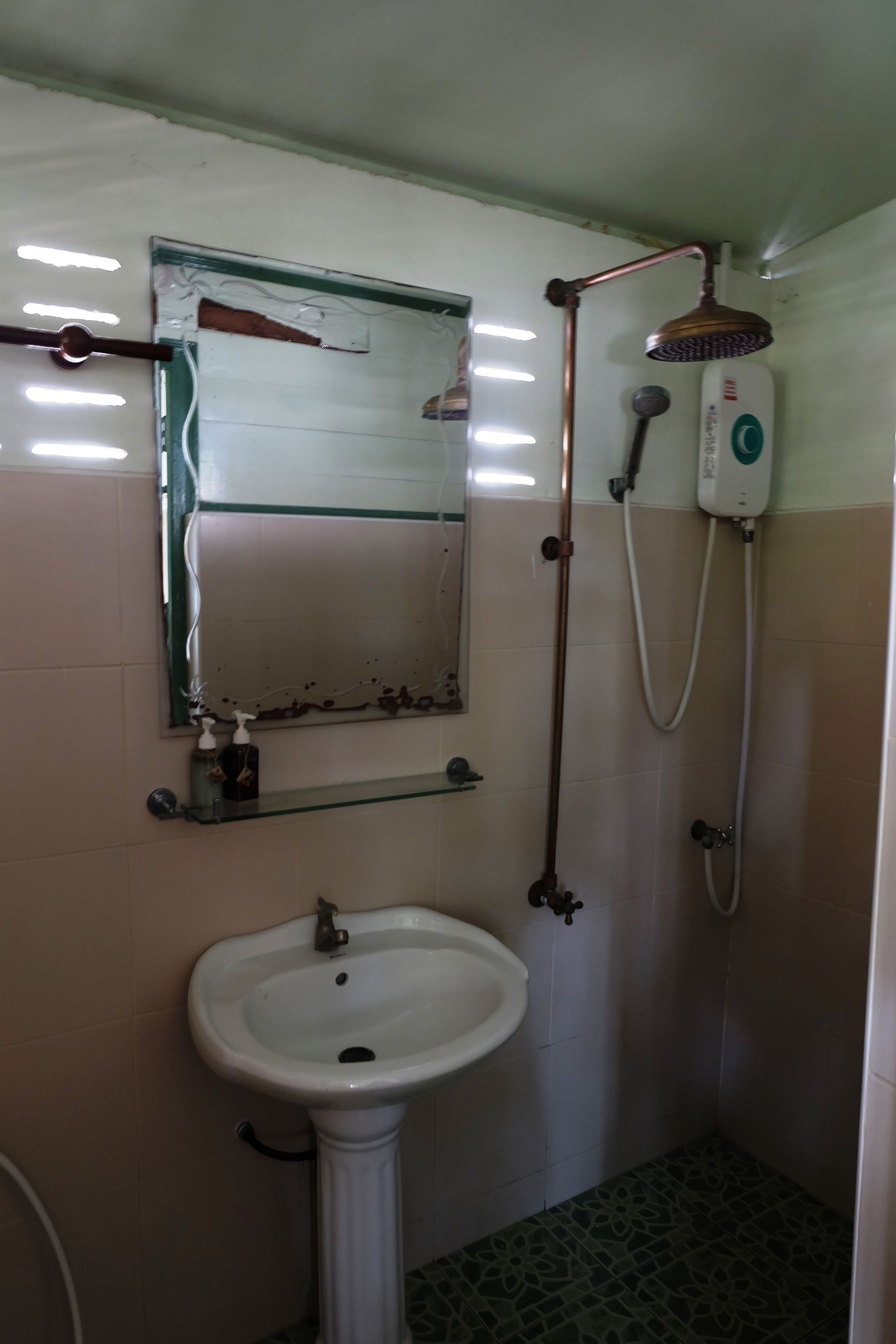 Un bagno con un lavandino su piedistallo, uno specchio con la cornice danneggiata, un soffione e un doccetta.