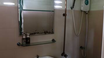 Un baño con lavamanos pedestal, un espejo con marco dañado, un cabezal de ducha y un accesorio de ducha manual.