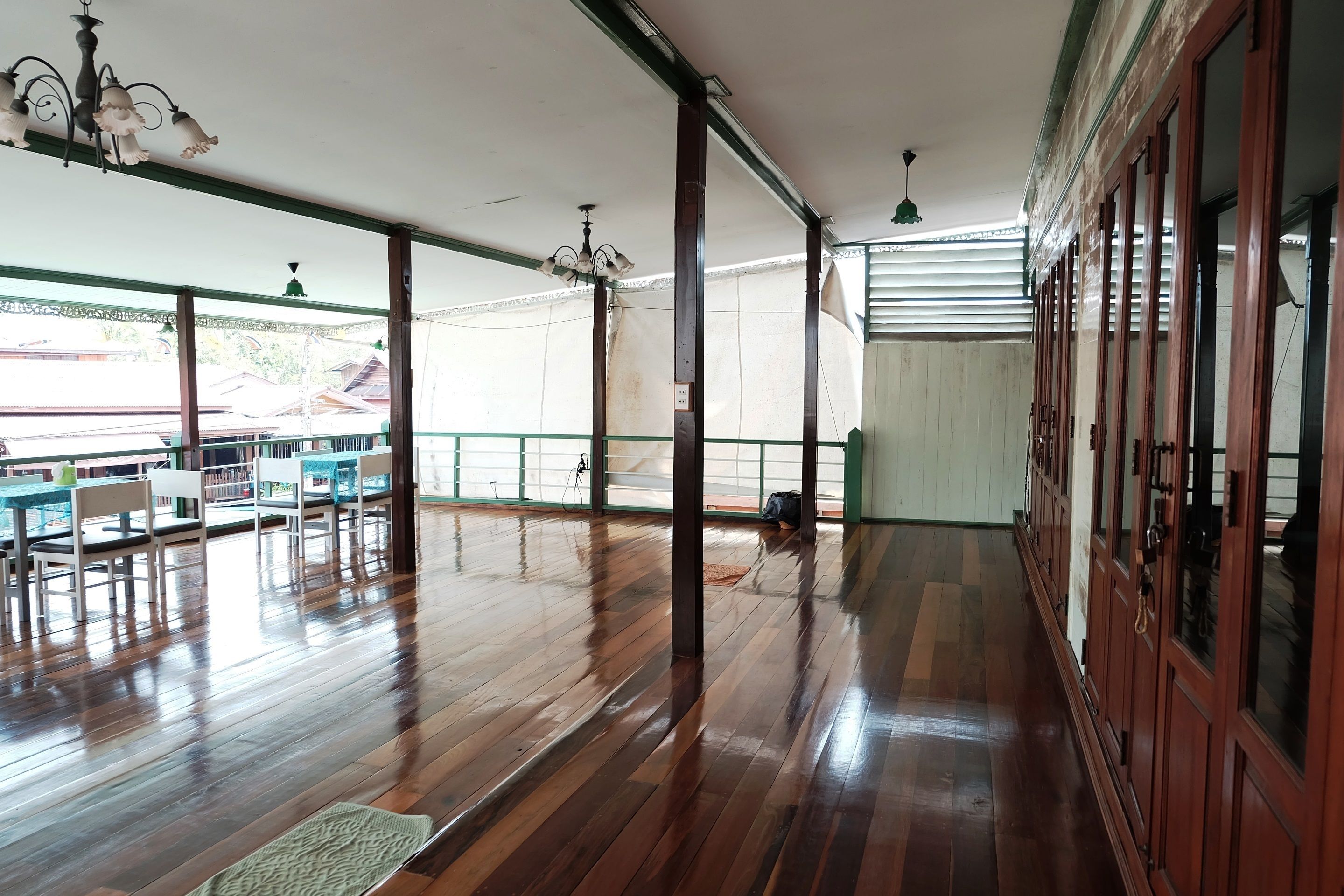 Una habitación amplia con suelo de madera, una zona de comedor con mesas y sillas, y ventanas grandes que dejan entrar luz natural.