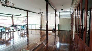 Una habitación amplia con suelo de madera, una zona de comedor con mesas y sillas, y ventanas grandes que dejan entrar luz natural.