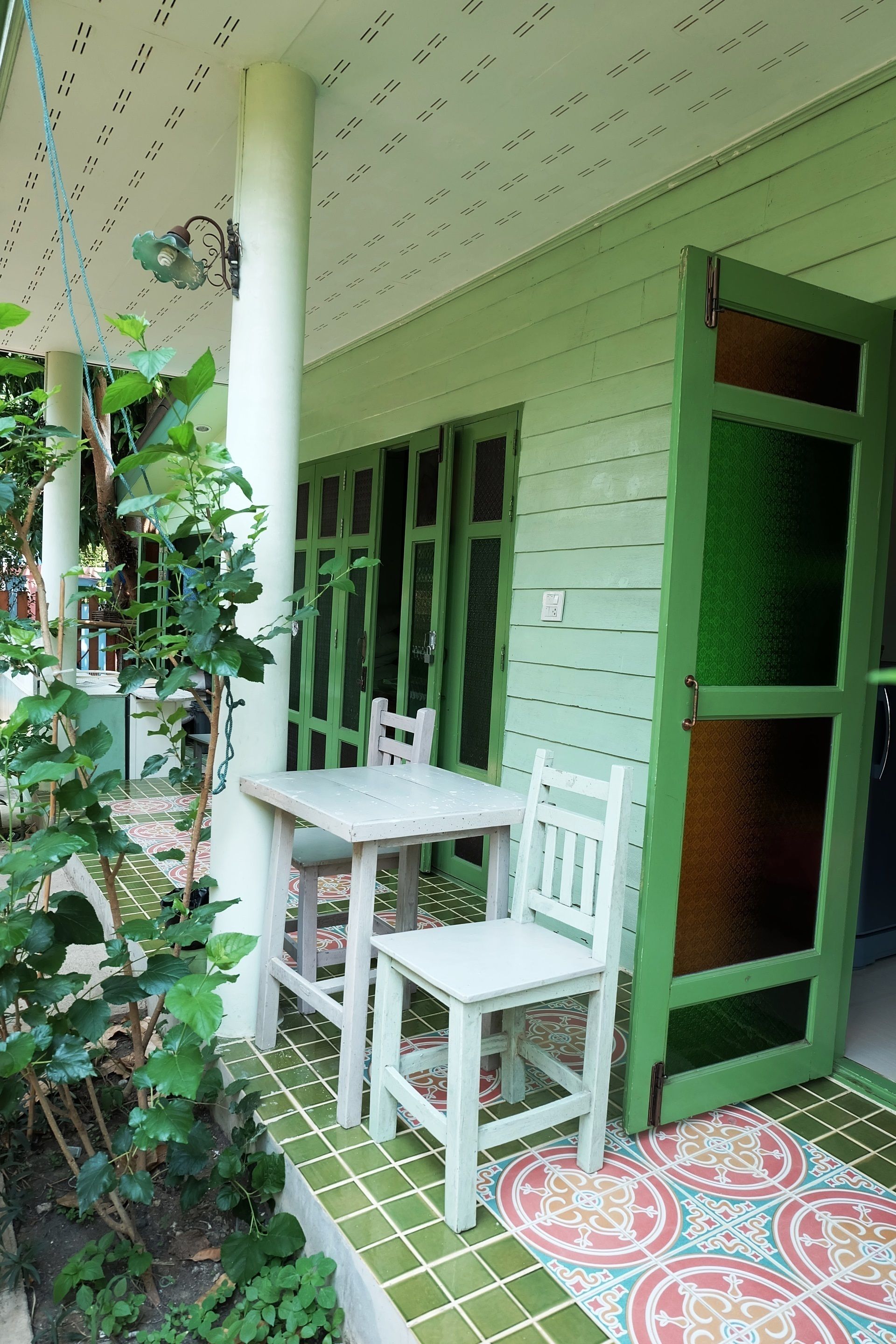 A green door with a glass panel, a white table with a chair, and a tiled floor with a pattern.