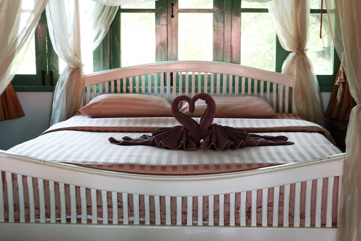 A bed with a heart-shaped towel arrangement, a striped bedspread, and a white headboard.