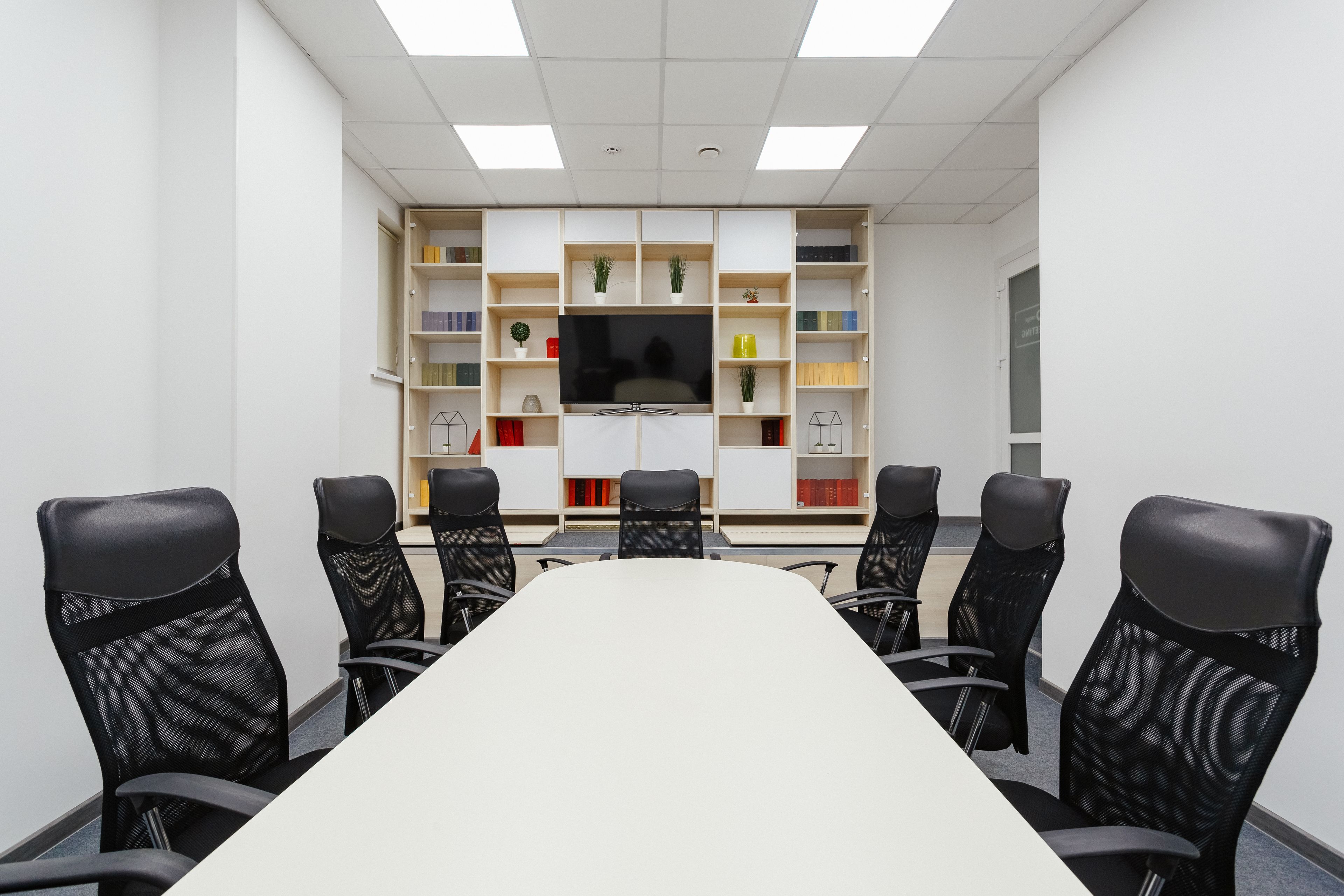 A conference room with a long table and six chairs, surrounded by shelves with books and decorative items.