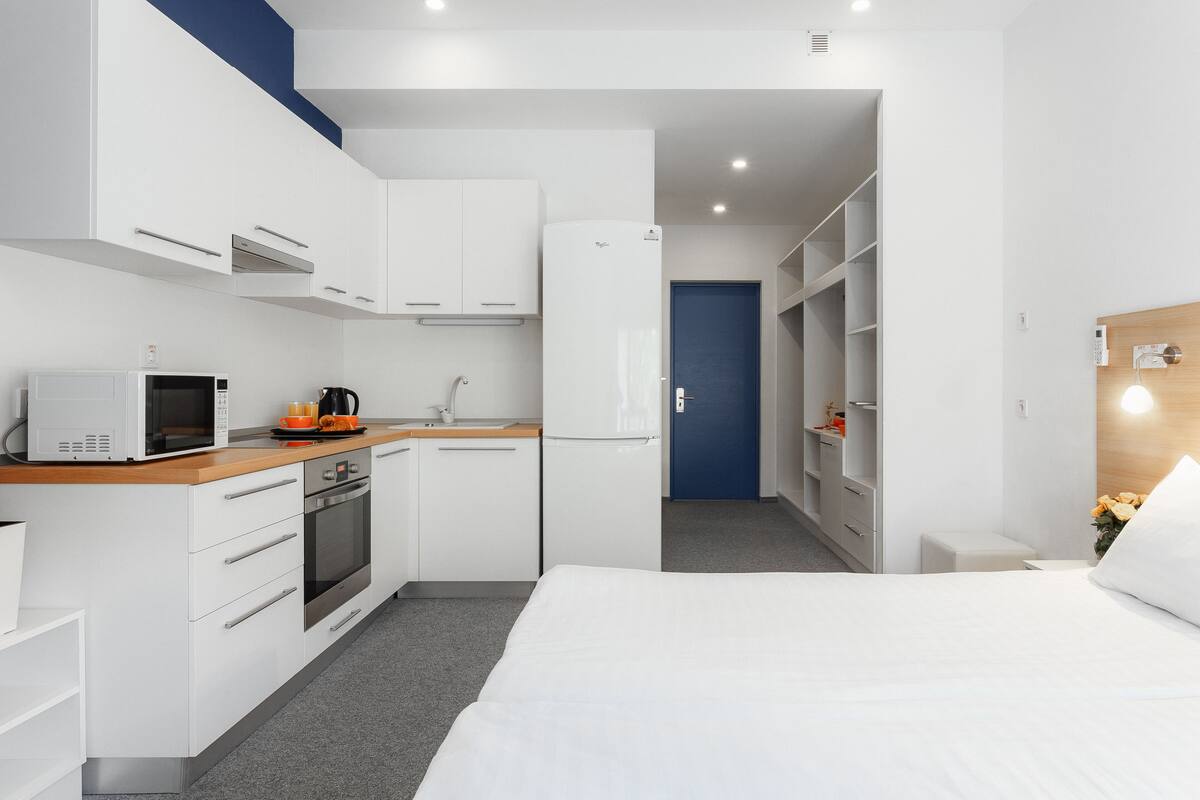 Una habitación de hotel pequeña con kitchenette, una cama, armario y baño reducido.