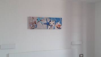 Una habitación de hotel con una cama, una mesita de noche pequeña y una obra de arte en la pared con estrellas de mar y conchas.