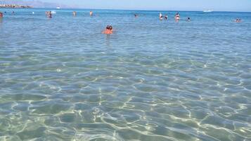 Una playa despejada con gente nadando y un barco a lo lejos.