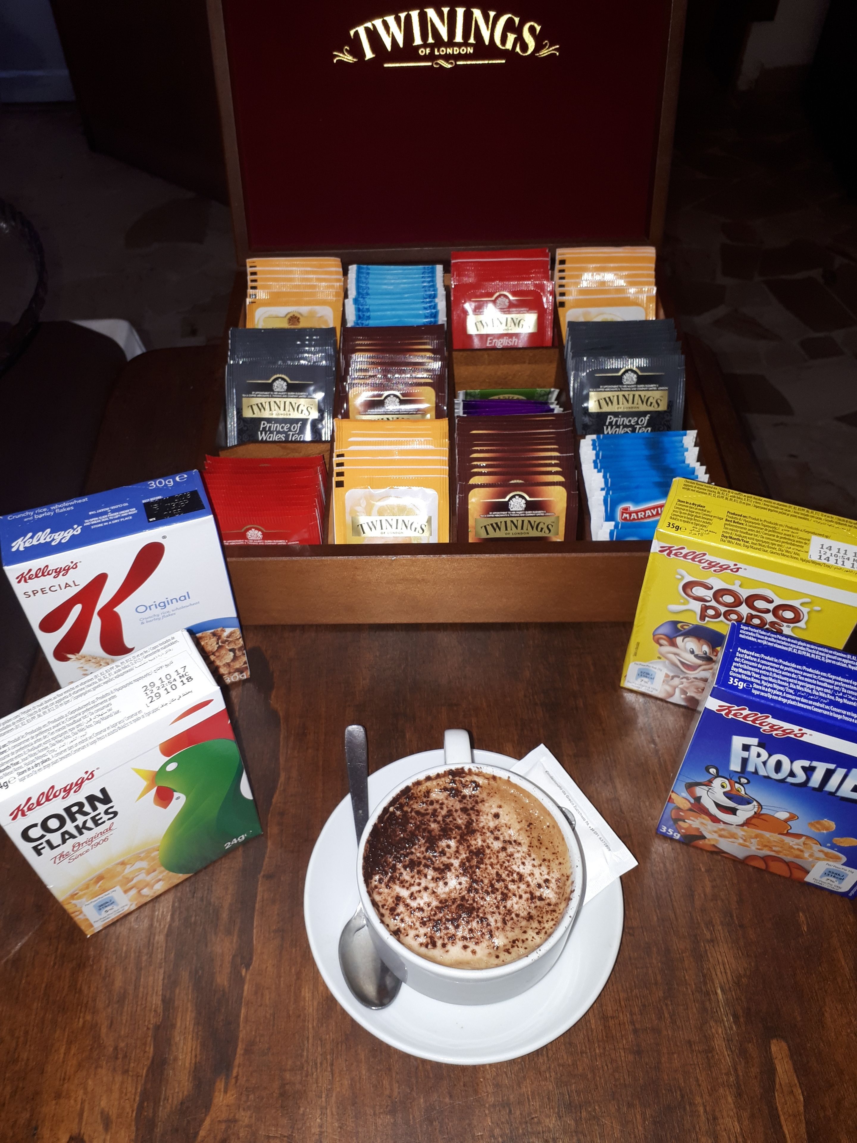 Pöydällä on tarjotin, jossa on useita Twinings-teepakkauksia, pakkaus Kellogg’s Frosted Flakes -muroja, pakkaus Kellogg’s Corn Flakes -muroja ja kuppi kahvia.