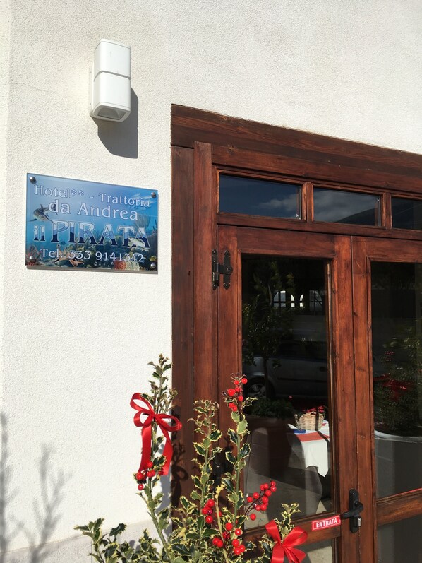 A wooden door with a glass panel, a signboard with hotel name and contact, and a potted plant with red berries.