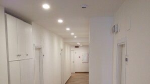 A long, narrow hallway with wooden flooring and white walls. There are multiple doors along the hallway, some with handles and others with keyholes. The hallway is well-lit with ceiling lights. - Hotel Il Pirata (Cinisi)