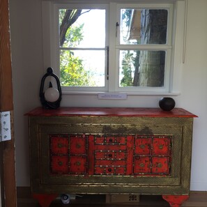 A red and gold cabinet with multiple drawers, a white window above it, and a small black object on top.