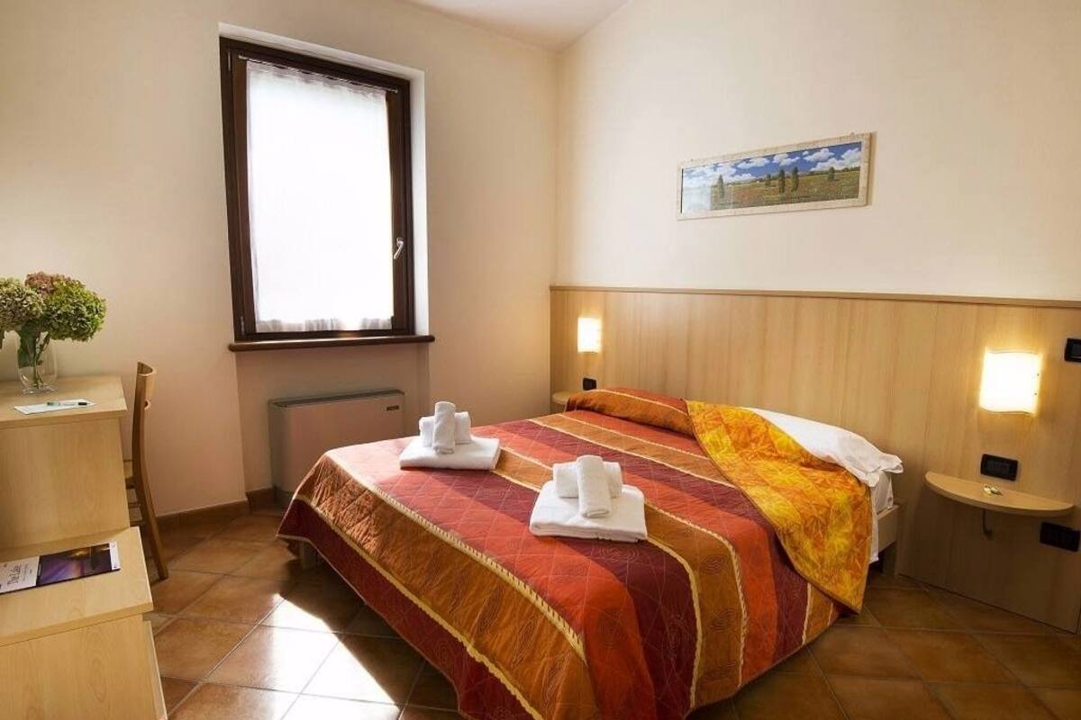 Une chambre d’hôtel avec un lit, un bureau, une chaise, une fenêtre et un tableau au mur.