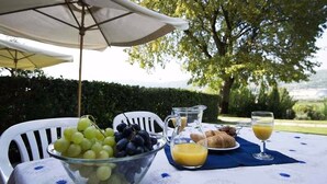 Una mesa dispuesta al aire libre con un cuenco de uvas, una jarra de zumo de naranja, croissants y un vaso de zumo de naranja.