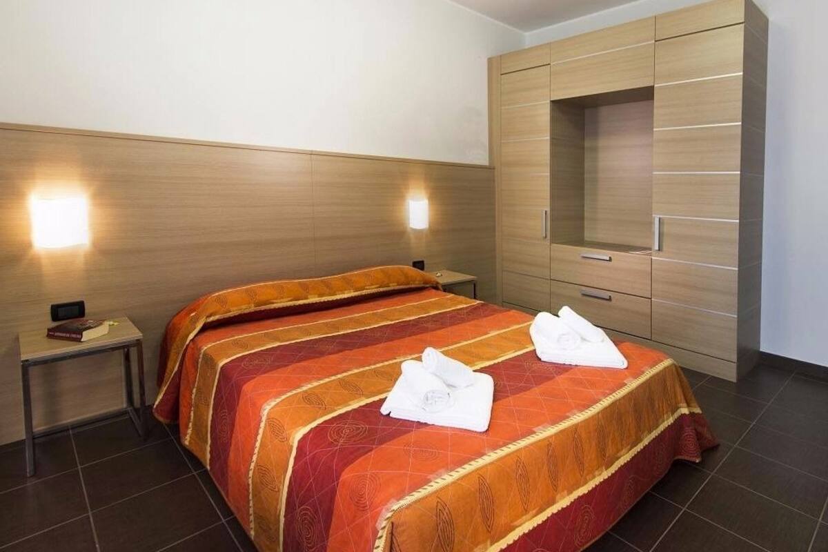 Une chambre d’hôtel avec un grand lit, deux tables de chevet, une armoire et un téléviseur fixé au mur.