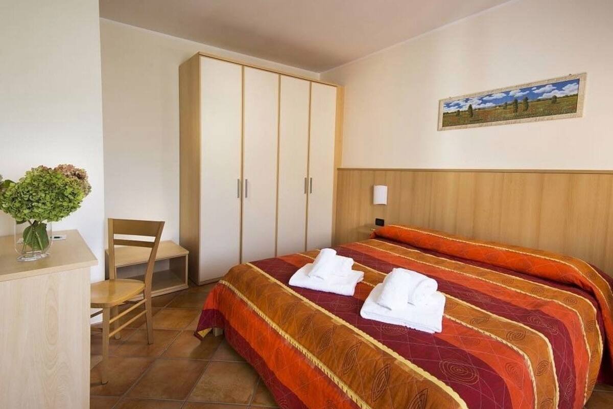 Une chambre d’hôtel avec un lit, un bureau, une chaise et une armoire.