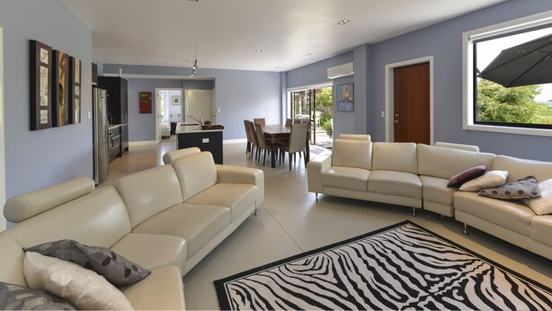 A spacious living room with a beige sectional sofa, a zebra-patterned rug, and a dining area with a wooden table and chairs. - Lakefront Holiday Home (Okere Falls)