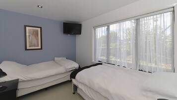 A hotel room with two single beds, a flat-screen TV mounted on the wall, and a window with sheer curtains.