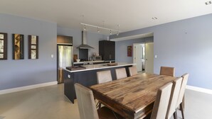 A spacious kitchen with a central island, modern appliances, and a dining area with a wooden table and chairs. - Lakefront Holiday Home (Okere Falls)