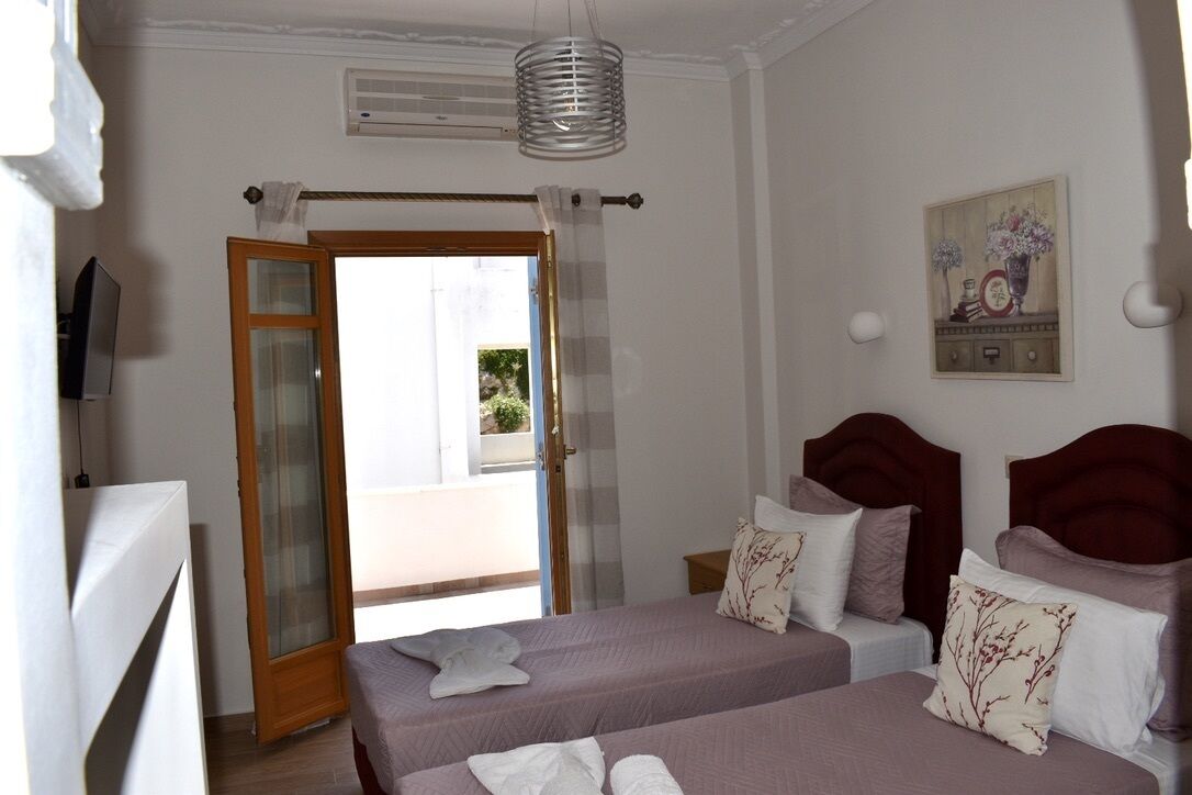 A bedroom with two beds, a wooden door leading to a balcony, a ceiling fan, and a wall-mounted picture.