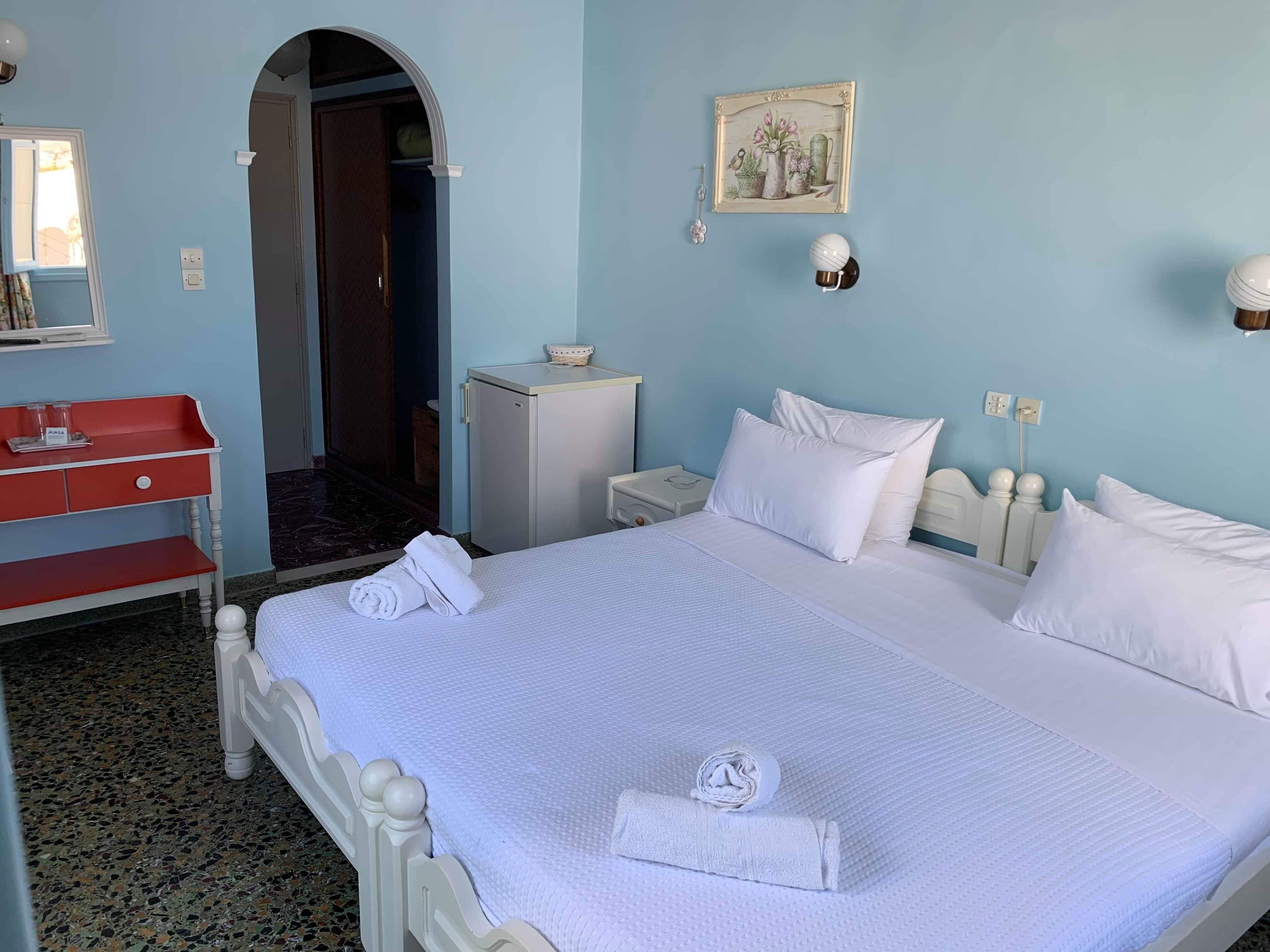 Habitación de hotel con una cama grande, un escritorio rojo, un armario pequeño y una puerta que da a otra habitación.