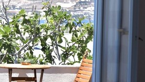 A room with a bed, a wooden chair, a small table, and a view of a mountain.